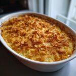 A baked cheesy potato casserole in a white oval dish, topped with a golden, crunchy cornflake crust.