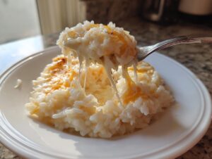 A fork lifting a scoop of creamy, cheesy rice, showing long, gooey cheese strings stretching from the main serving.