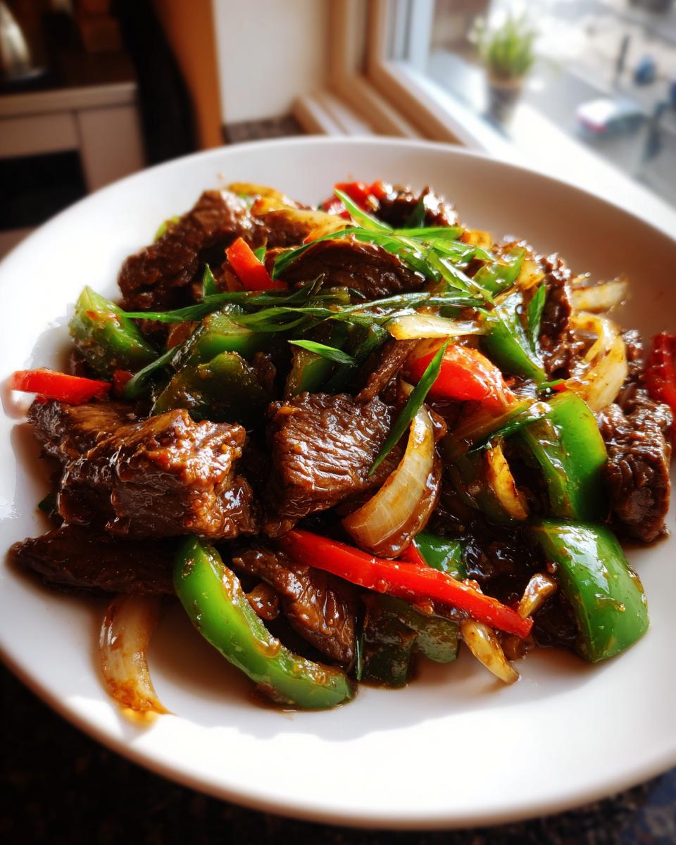 A close-up of glistening Chinese pepper steak featuring tender beef, green bell peppers, red peppers, and onions, garnished with scallions.