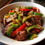 A close-up, appetizing shot of freshly cooked Chinese pepper steak featuring tender beef strips mixed with bright green and red bell peppers.