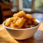 Close-up of chunky homemade applesauce topped with cinnamon served in a white bowl.