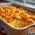 Close-up of a baked cream cheese corn casserole topped with golden, crunchy cornflakes in a white baking dish.