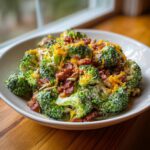 A bowl filled with creamy broccoli salad topped generously with bacon bits, shredded cheddar cheese, and sunflower seeds.