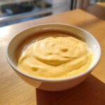 A close-up of rich, creamy cheese fondue with a smooth, slightly bubbly surface in a white bowl.