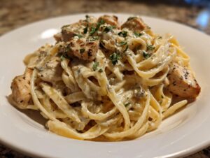 A close-up of creamy fettuccine pasta tossed in Alfredo sauce with seasoned, cubed chicken pieces, garnished with parsley, making delicious chicken alfredo.