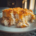 A close-up serving of creamy chicken and rice casserole topped with melted cheddar cheese and a crispy breadcrumb crust.