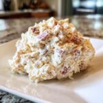 A close-up of a generous scoop of creamy ham salad recipe mixed with diced ham, served on a square white plate.