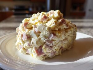 A mound of creamy ham salad recipe featuring diced ham and eggs, served on a white plate.