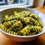 Close-up of creamy pesto pasta made with fusilli in a white bowl, showing vibrant green sauce.