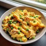 Close-up of creamy tuna pasta mixed with bright green peas served in a light gray bowl.