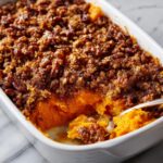 A spoonful being taken from an easy sweet potato casserole topped with a rich, brown sugar and pecan crumble.