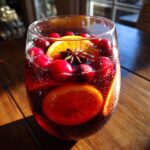 Close-up of a glass filled with vibrant red holiday sangria, garnished with fresh cranberries, orange slices, and star anise.
