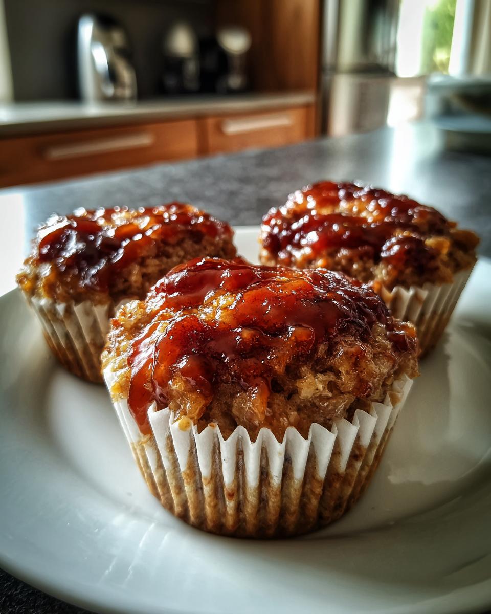 Three individual mini meatloaf portions baked in white paper liners, topped with a shiny brown glaze.