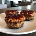 Three individual mini meatloaf portions topped with a shiny, dark red glaze, served on a white plate.