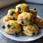 A tall stack of fluffy lemon blueberry scones drizzled with a thick lemon glaze, garnished with fresh blueberries.