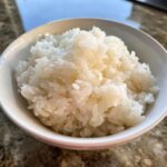 Close-up of perfectly cooked, fluffy white sushi rice served in a small white bowl.