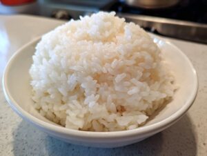 Close-up of a perfectly mounded serving of glossy, white sushi rice in a small white bowl.