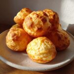 A stack of freshly baked, golden brown brazilian cheese bread puffs sitting on a speckled ceramic plate.