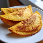 Three golden, crispy fried potato tacos resting on a white plate, ready to be filled.