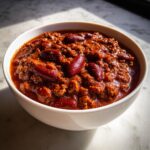 Close-up of a white bowl filled with rich, thick homemade chili featuring ground meat and dark red kidney beans.