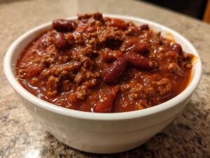 Close-up of a white bowl filled with rich, thick chili featuring ground meat and visible kidney beans.