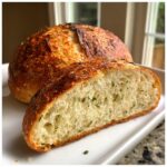 A close-up view of a freshly baked artisan bread loaf, sliced open to show the airy crumb dotted with herbs.