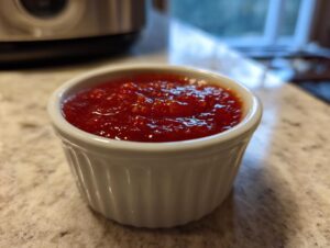Close-up of vibrant red homemade cocktail sauce served in a small white fluted ramekin.