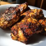 Close-up of perfectly cooked chicken pieces coated in a dark, flavorful chicken marinade, showing charred edges.