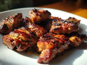 Close-up of beautifully caramelized and slightly charred chicken pieces coated in a rich chicken marinade, served on a white plate.