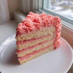 A close-up slice of a layered rose cake featuring vanilla sponge and pink filling, topped with piped pink frosting.