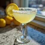 A bright yellow Lemon Drop martini in a coupe glass with a thick sugar rim and lemon slice garnish.