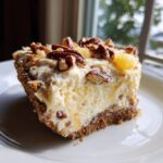 A generous slice of creamy Million Dollar Pie with a graham cracker crust, topped with pecans and pineapple chunks.