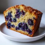 Close-up of a moist slice of blueberry breakfast cake with a golden, sugary crust.