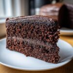 Close-up of a slice of moist chocolate cake showing its rich, dark crumb and glossy chocolate frosting.
