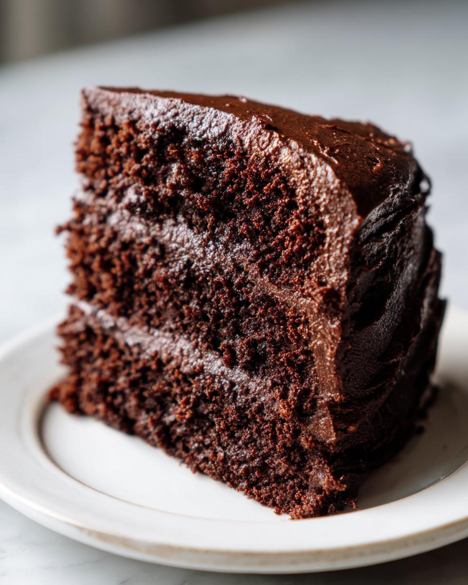 A close-up of a thick slice of moist chocolate cake layered with rich chocolate frosting.