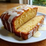 A loaf of moist lemon zucchini bread, sliced open, covered in thick white lemon glaze.