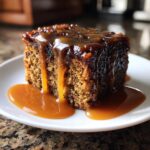 A close-up of a square slice of moist sticky toffee pudding recipe drenched in rich caramel sauce.
