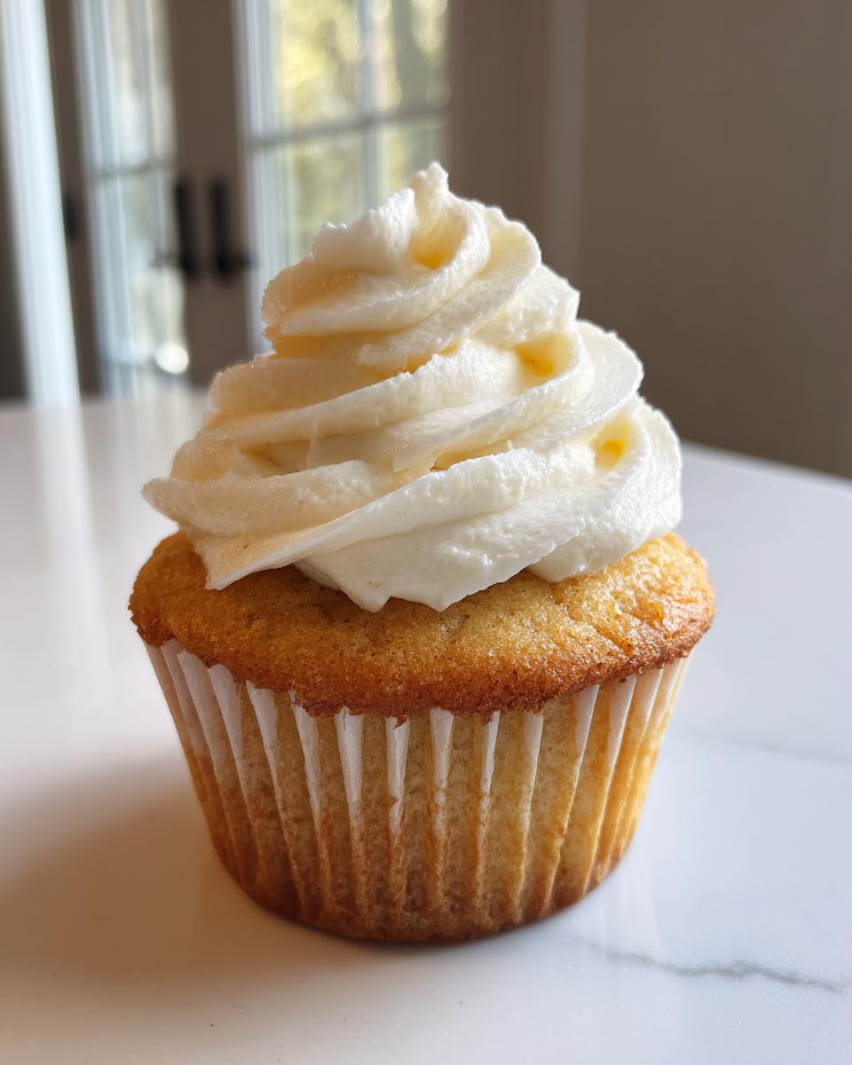 A single, moist vanilla cupcake topped with a generous swirl of white vanilla buttercream frosting.