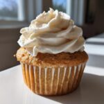 A single, perfectly baked vanilla cupcake topped with a generous swirl of creamy white vanilla frosting.