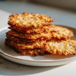 A stack of five golden brown, crispy oatmeal lace cookies piled on a light ceramic plate.