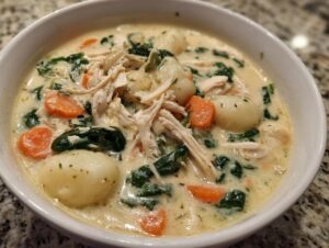 Close-up of a bowl of creamy Olive Garden Chicken Gnocchi Soup featuring shredded chicken, spinach, carrots, and potato gnocchi.