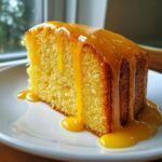 A moist slice of orange juice cake topped with a thick, dripping orange glaze, served on a white plate.