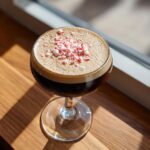 A rich peppermint espresso martini in a coupe glass, topped with a mound of crushed red and white candy canes.