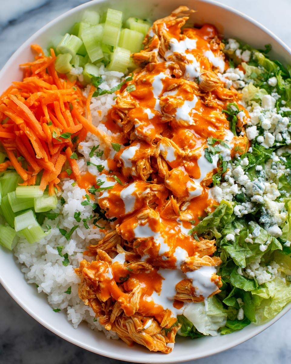 Close-up of a vibrant buffalo chicken bowl featuring shredded chicken coated in orange sauce, white rice, celery, carrots, and blue cheese crumbles.