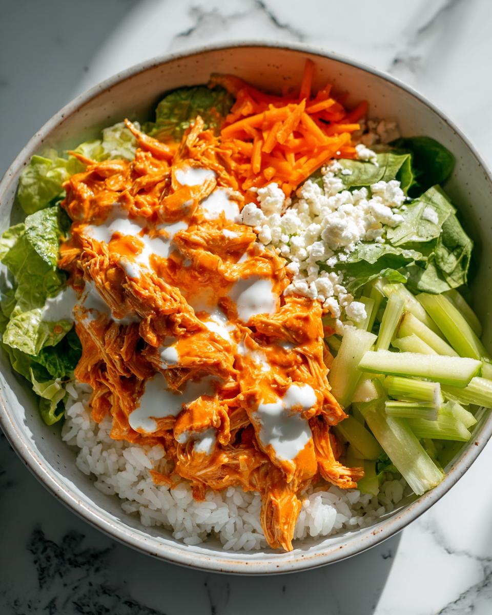 Overhead view of a quick buffalo chicken rice bowl topped with shredded orange buffalo chicken, ranch dressing, celery, carrots, and blue cheese.