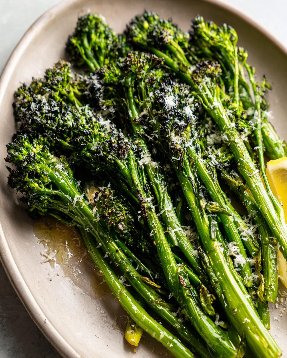 Close-up of bright green, roasted broccolini topped with grated Parmesan cheese and a lemon wedge.