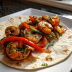 Close-up of seasoned shrimp, red and green bell peppers, and onions served on a soft flour tortilla for shrimp fajitas.