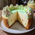 A slice cut from a creamy Christmas tree cheesecake featuring a light green topping, whipped cream, and colorful sprinkles.