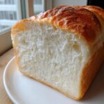 Close-up of a freshly baked milk bread loaf, showing its incredibly soft, white interior crumb and golden crust.