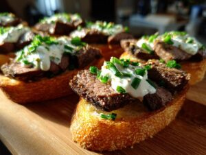 Close-up of several steak crostini appetizers topped with seared steak, creamy sauce, and fresh chives.